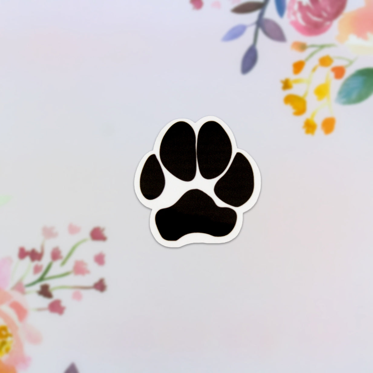 The Puppy Paw Sticker gracefully rests on a light backdrop, embellished with vibrant floral patterns. Ideal for dog enthusiasts, this decorative sticker brings a playful charm to any surface.