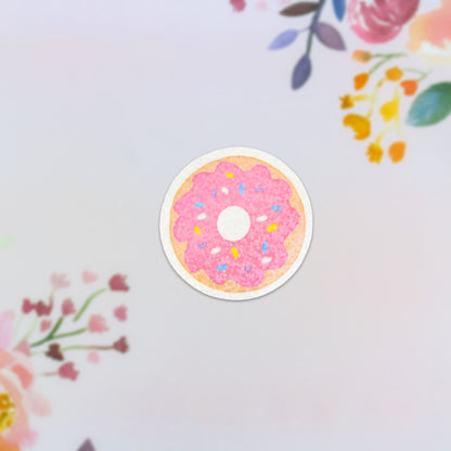 The Strawberry Donut Holographic Sticker showcases a pink frosted donut topped with vibrant sprinkles, all set against a light pastel background embellished with floral designs in hues of pink, orange, and purple. This sticker is dishwasher safe, ensuring long-lasting enjoyment.